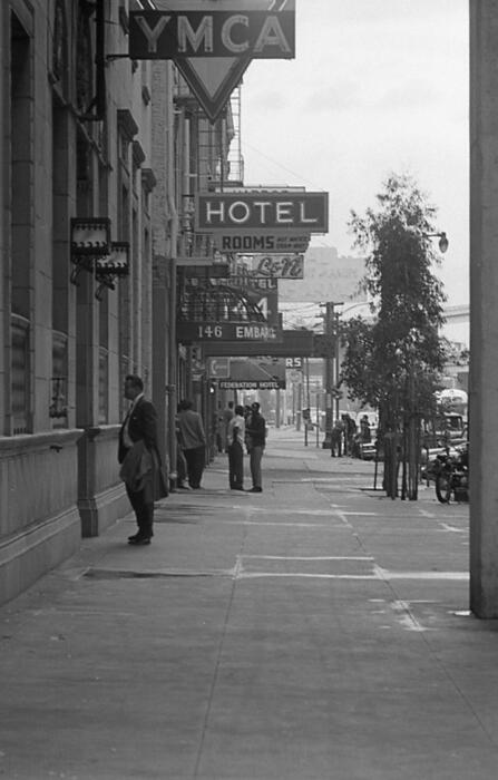 [View of hotel and business awnings and signs, and people on the 100 block of Embarcadero, YMCA in foreground]