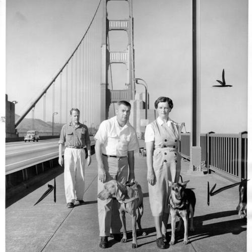 [Max Heierle giving instruction on Golden Gate Bridge to Fraser Brown and Mrs. Grace Petrie in training guide dogs for the blind]