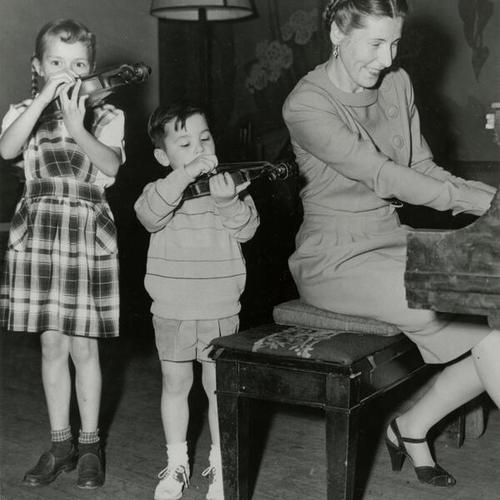 [Two children playing violin and teacher Margaret Jensen playing piano]