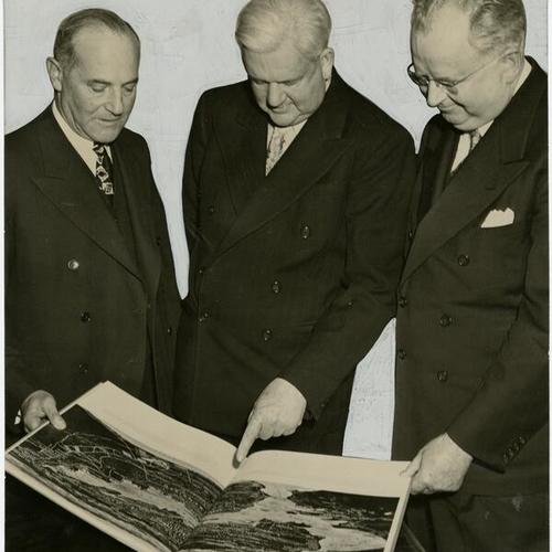 [Walter Haas (left), Mayor Lapham (center) and Dr, Henry F. Grady looking at an illustrated brochure showing the advantages of the Bay Area]