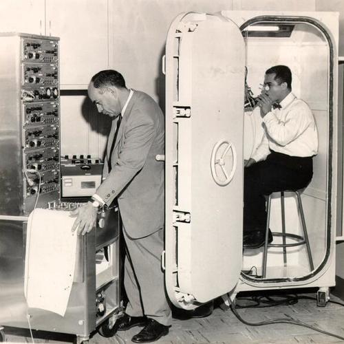 [Dr. Julius H. Comroe Jr. and Dr. Santiago Guzman testing a physiological "isolation booth" at U. C. Medical Center]