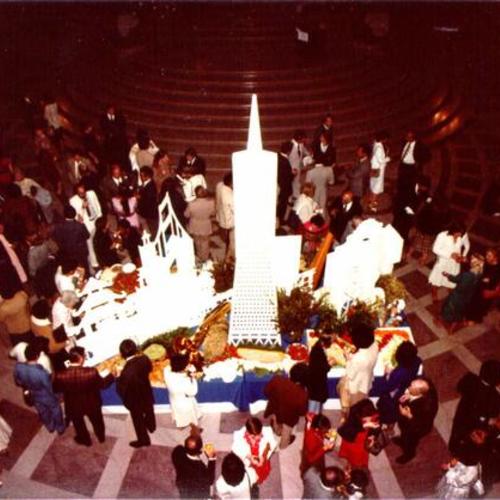 [Group of people gathering around a miniature structure of San Francisco located in the Rotunda of City Hall]