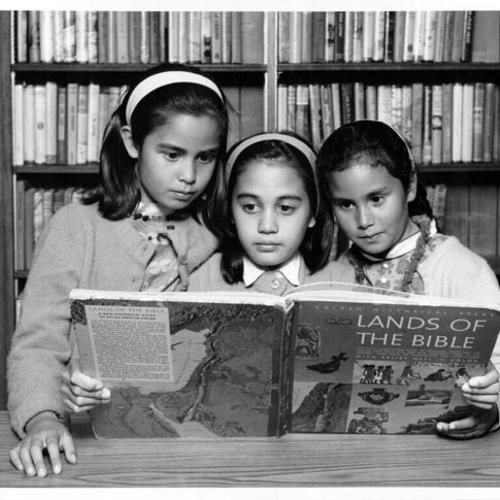 [Three girls reading a book at Eureka Valley Branch Library]