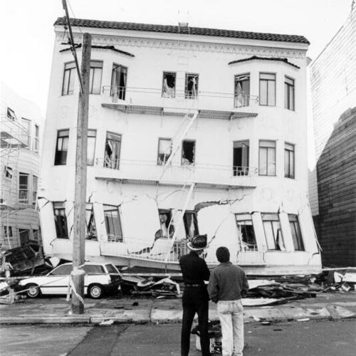 [Two people standing in front of a building destroyed in the October 17, 1989 Loma Prieta earthquake]