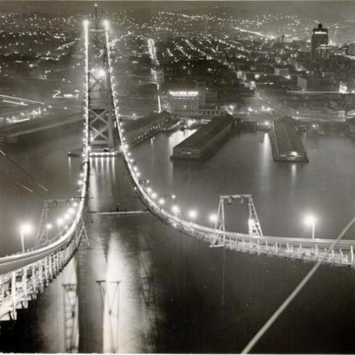 [View of the San Francisco-Oakland Bay Bridge while under construction showing suspension bridge catwalk between San Francisco and Yerba Buena Island]