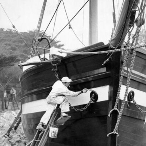[Melvin W. Brown applies paint to bow of the Gjoa, famed Norwegian ship in which Dr. Roald Amundsen negotiated the Northwest Passage between 1903 and 1906]