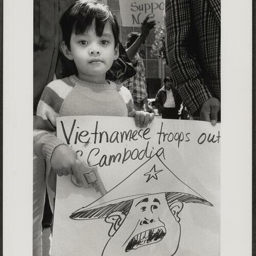 Cambodians and child with toy gun and sign protesting for Vietnamese withdrawal from Cambodia outside Federal Building