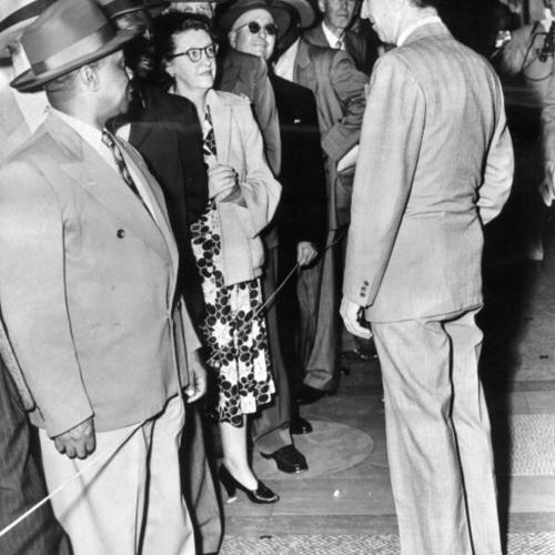 [Harry Bridges, right, pauses in the corridors of the Post Office Building to chat with members of the crowd which came to sit in on a federal Court hearing in which the Government is seeking to revoke Bridges' bail.]