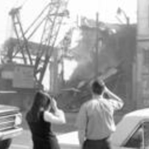 [Two people watch from across the street as building is demolished, part of South of Market Redevelopment, 