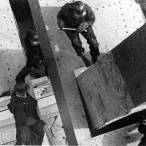 [Overhead view of construction workers attaching girder to north tower of Golden Gate Bridge]