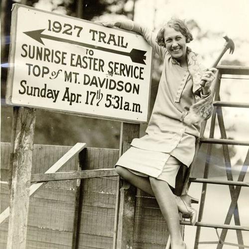 [Dorothie Valien posing next to a sign giving directions to Sunrise Easter Service on Mount Davidson]