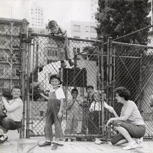 [Group of children trying to get past a fence at Michelangelo Playground]