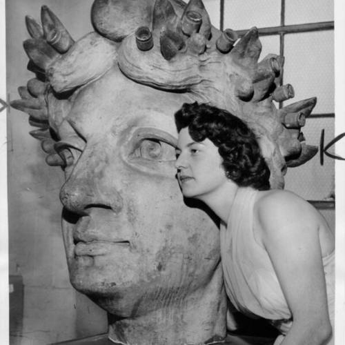 [Barbara Mennucci, queen of San Francisco's festival of progress, posing next to the head of what once was a statue of the Goddess of Liberty]