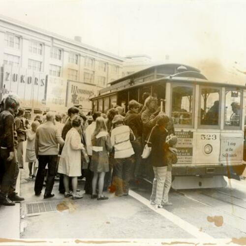 [Crowd of people boarding a cable car at Powell and Market streets]