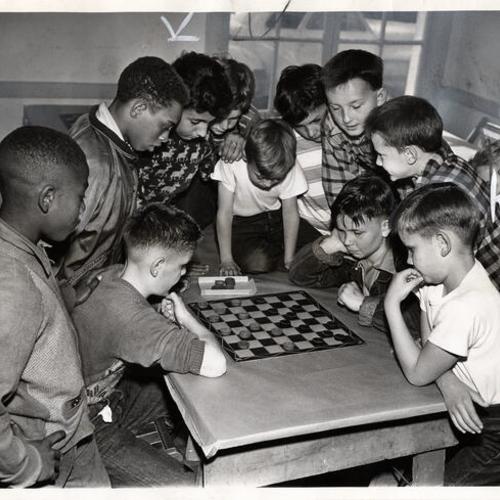 [Vern Rieger and James McCloud surrounded by spectators while playing a game of checkers at San Francisco Boys' Club in Mission district]