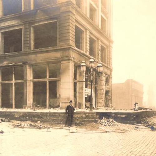 [Man in a top hat stands amongst earthquake rubble next to the Aetna Life Insurance building, at Spear and Market Streets, after the 1906 earthquake]
