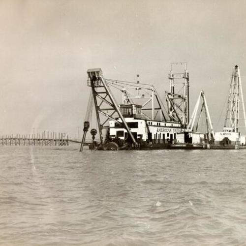 [View of American Dredging Company electrically dredging sand out of the port of Oakland harbor to build a sand fill for the San Francisco-Oakland Bay Bridge right of way]