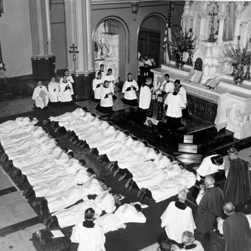 [Priests lying facedown on the ground in front of an altar at St. Mary's Cathedral during their ordination rites]