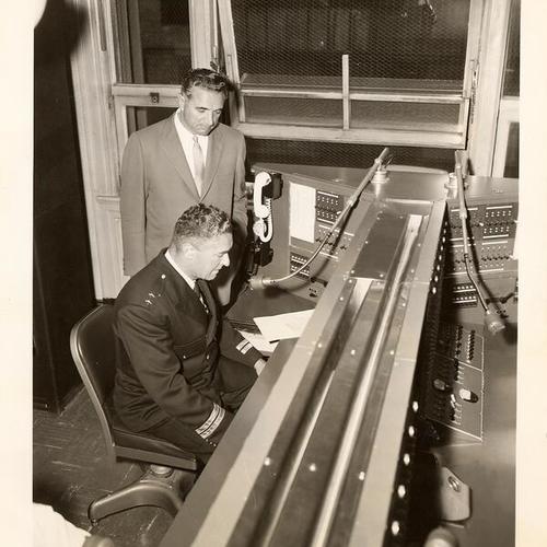 [Major George Christopher observing how Chief of Police Frank Ahearn operates the new police radio broadcasting console after extensive renovations were made in the Communications Room in Old Hall of Justice]