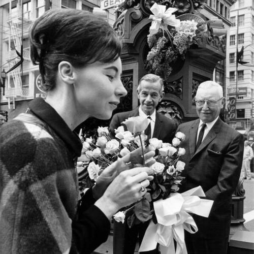[Gwen Curatilo sniffing a rose while floral designer Armin Wiskeman of Podesta Baldocchi and A. F. Podesta look on in the background]