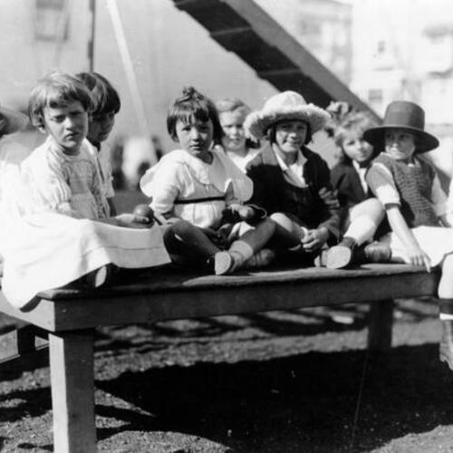 [Unidentified group of children sitting on a table in a playground]