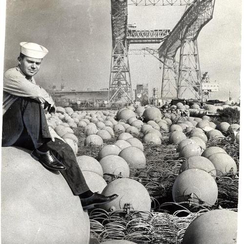 [Steve Matthews sitting in a field of floats, used to support harbor defense nets, at Hunters Point Naval Shipyard]