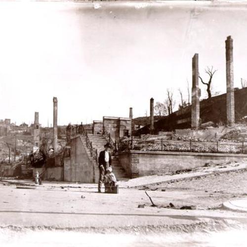 [Unidentified child and one other person standing in front of decimated buildings]