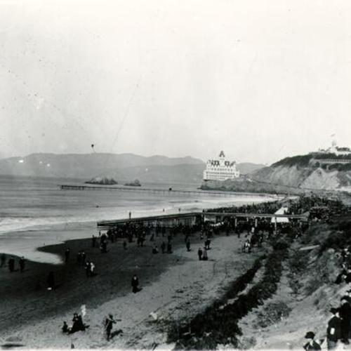 [Crowds of people gathering on Ocean Beach facing the Cliff House]