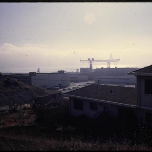 Overgrown vegetation on hillsides next to withered buildings with naval shipyard in background