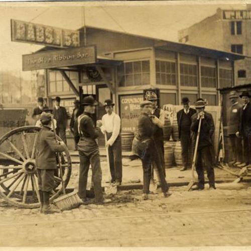 [Men and boys, some with brooms and shovels, standing outside of a bar after the 1906 earthquake]
