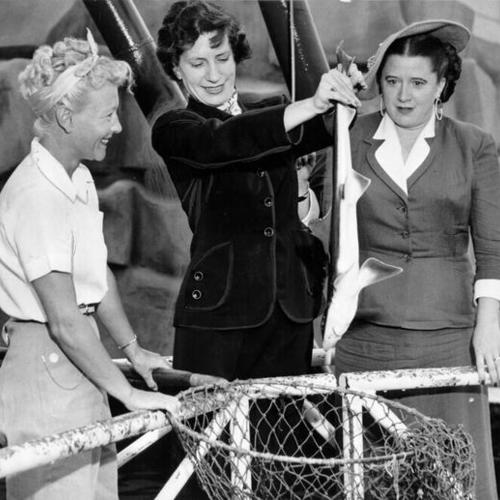 [Eleanor Montgomery and Virginia Johnson, of Polly's Shopping Service, inspecting a gray shark provided to them by Marian Martini  to be used to advertise sharkskin cloth suits for a men's clothing store on Kearny Street]
