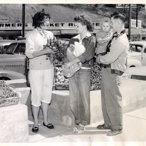 [Seller Audrey Ferraris showing her vegetables to Mr. and Mrs. A. L. Crouch and their daughter Sharon at the Farmers' Market on Alemany  Boulevard]