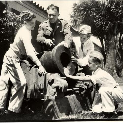 [Corporal B. G. Byrd showing three young boys an old cannon at the Presidio]