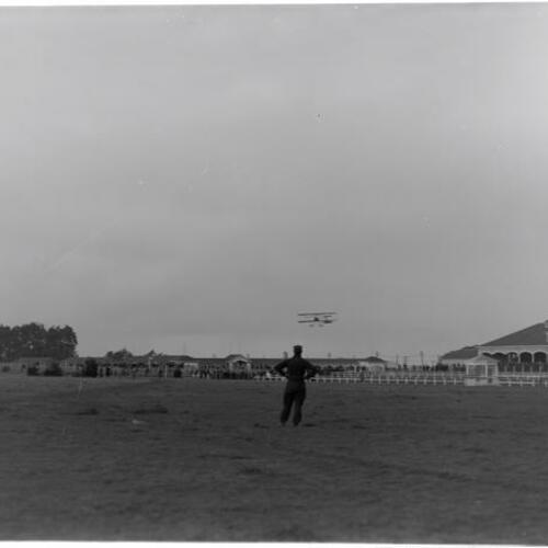 Louis Paulhan watching biplane fly at Tanforan racetrack stadium