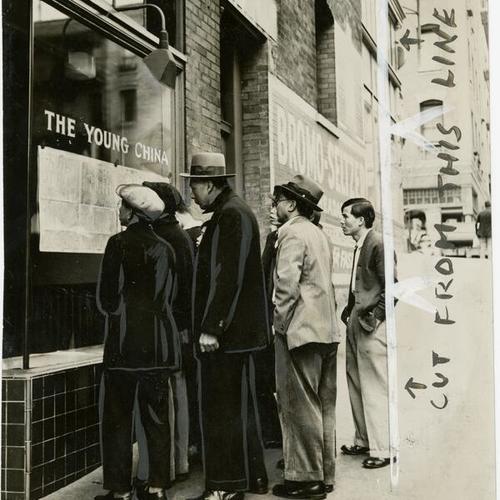 [Group of men looking at a newspaper outside of The Young China in Chinatown]