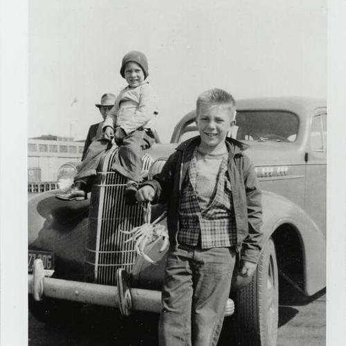 [Charlie holding a crab and brother Angelo sitting on top of car with grandfather Charles at Pier 43, Fisherman's Wharf]
