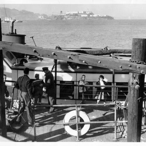 [Group of people boarding a boat at San Francisco waterfront, with Alcatraz Island visible in background]