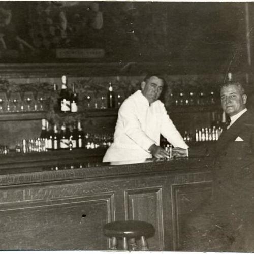 [Bartender Stanley Sliter pouring Palace Hotel manager A. H. Price a drink at the Happy Valley bar]