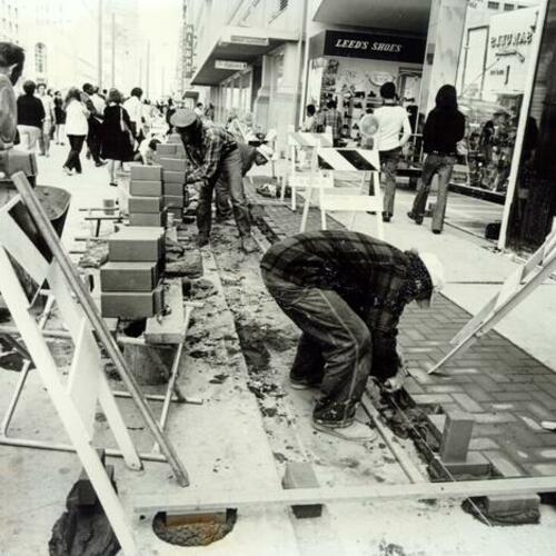 [Construction workers laying bricks on the sidewalks of Market Street]