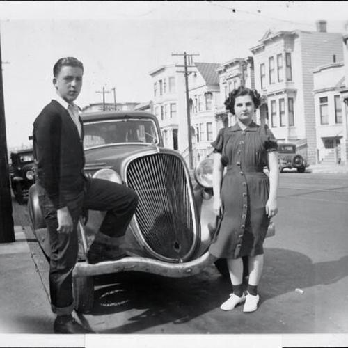 [Portrait of a young woman and her brother next to car]