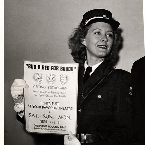 [American Women's Voluntary Services (AWVS) volunteer holding sign 'Buy a Bed for Buddy']