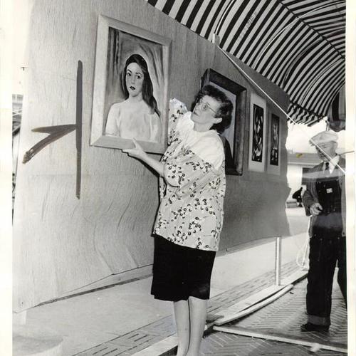 [Mildred Pommer hanging a painting that will be displayed at a Civic Center art exhibit]