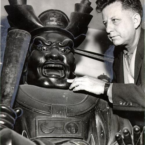 [John G. Saxby, owner of the Pacific Curio Shop, inspecting a Japanese sculpture for sale there]
