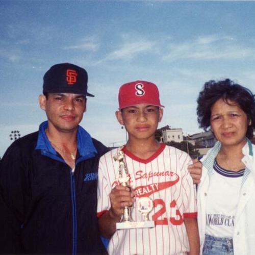 [Joel at All Star baseball game at Jackson Playground with his parents while being awarded for hitting grand slam and winning the game]