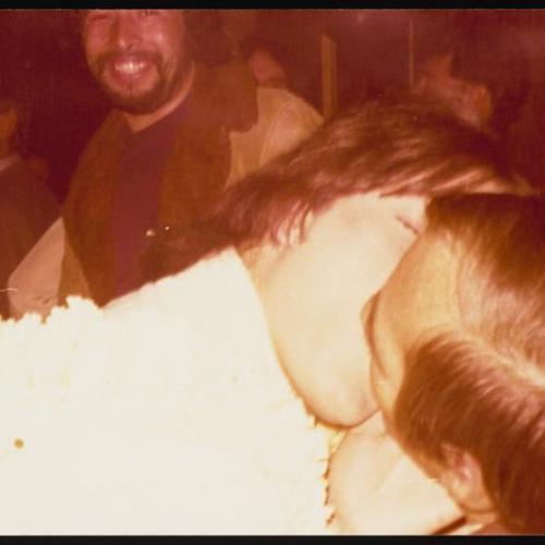 Two people kissing at Jim and Ken's wedding party with person smiling in background