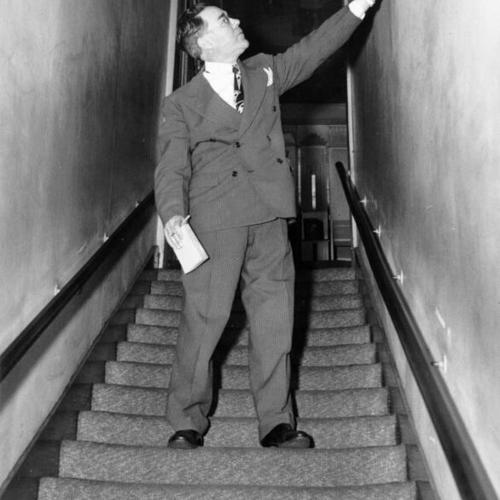 [James J. Sullivan looking over narrow front stairwell at Finocchio's nightclub during a fire inspection]