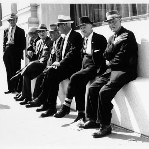 [Group of men leaning against the side of a building on Market Street in the Tenderloin District]
