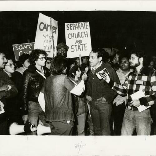 [Harvey Milk interviewed at a rally, Cleve Jones stands to left of television reporter]