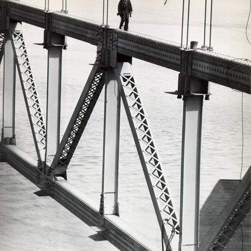 [Worker walking along a steel structure during construction of the San Francisco-Oakland Bay Bridge]