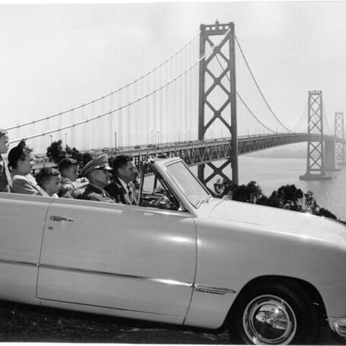 [Highway patrol Captain R. C. Wilkinson rides with Warren E. Webb and family on Yerba Buena Island with Bay Bridge in background]